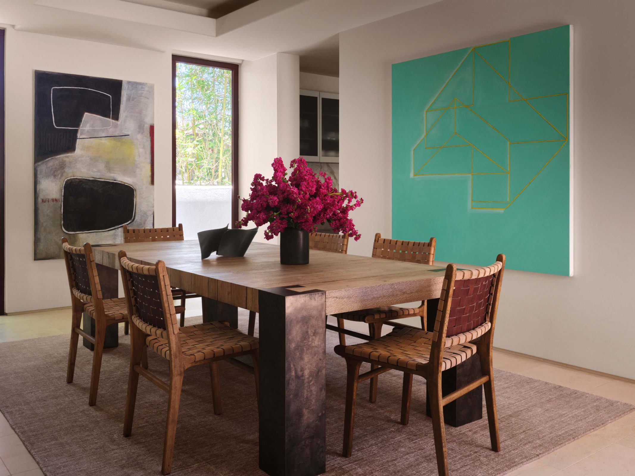 Dining room with a wood table, woven leather chairs and two large Lori Brunner paintings, photographed by Douglas Friedman