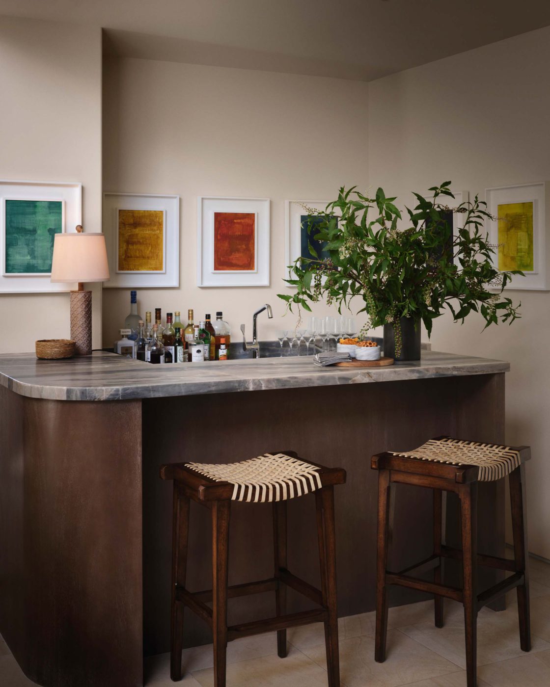Bar with a marble counter, woven stools and a row of six tonal Lori Brunner paintings