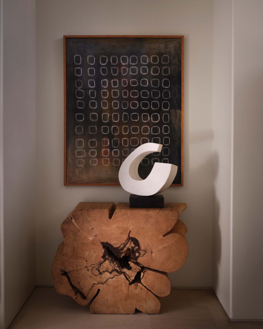 Entry niche with a dark Lori Brunner painting above a white sculpture on a wood-slab bench