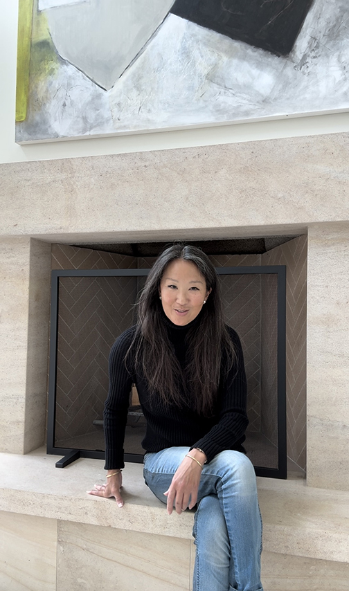 Lori Brunner seated in the stone fireplace niche below one of her paintings